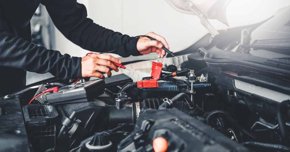 Man looking at auto parts under a car's hood.